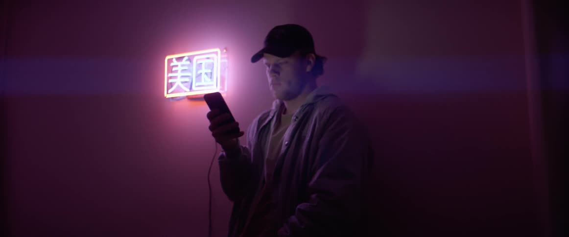 Man leans against wall near neon sign reading on phone