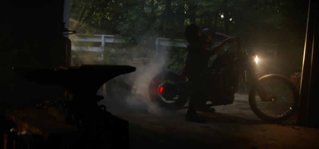 A man starts his motorcycle up and looks at the exhaust coming from it