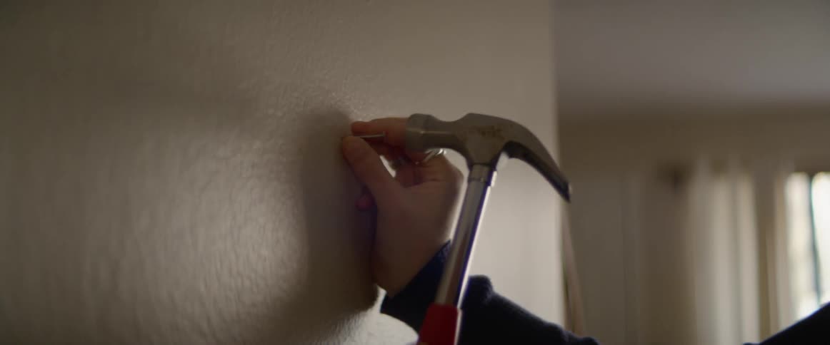 A woman holds a nail against a wall and hammers it in