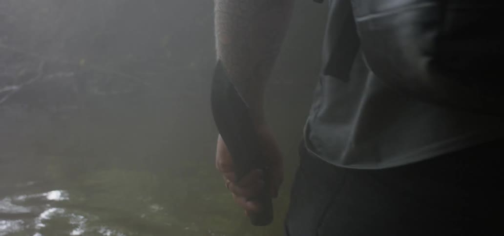A man holding a knife looks around the outdoors