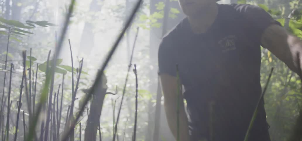 A man uses a knife to cut branches off of trees