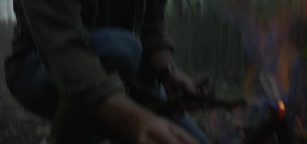 Two men adding wood to a campfire