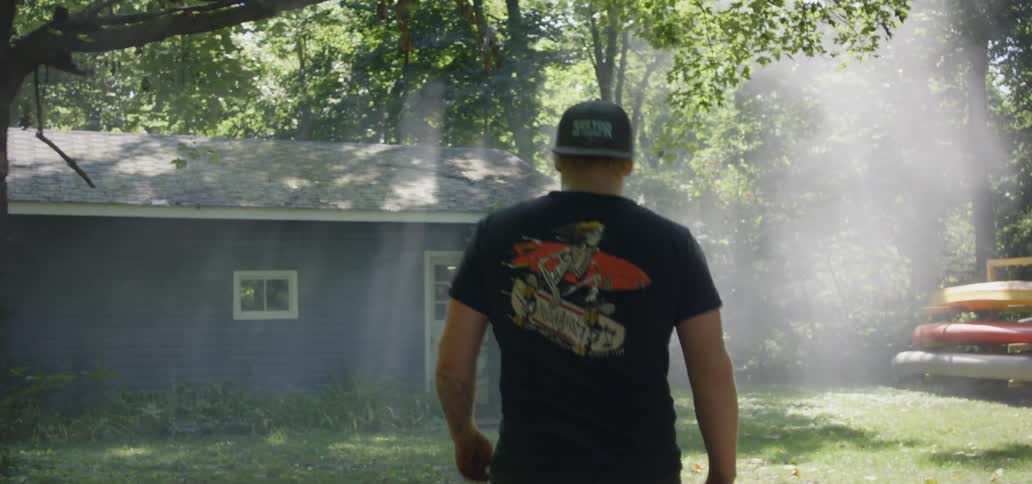 A man strides with determination towards a small house that is located within a forested area