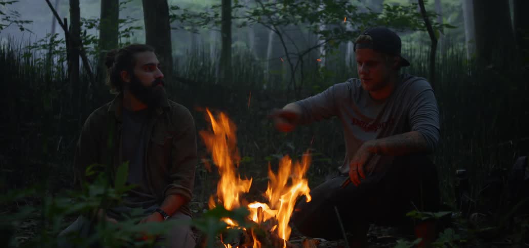 Two men sit outside by a campfire together