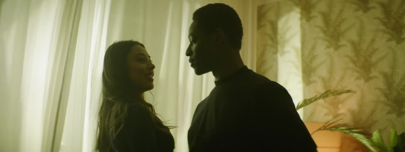 A man following a woman through a room before grabbing her wrist and pulling her around to face him