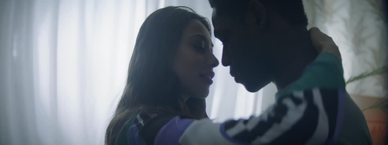 A young man and woman embrace in a dimly lit room