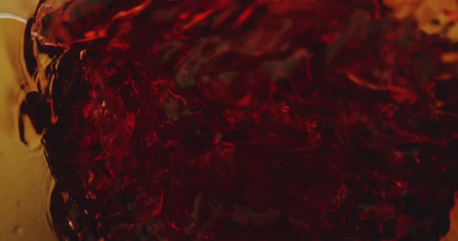 An red and amber hued liquid swirls and splashes as it is poured into a container