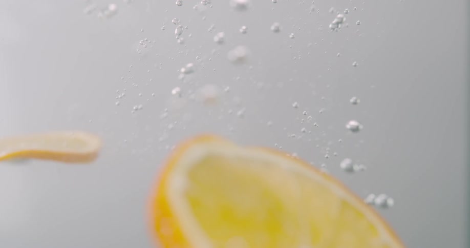 Slices of lemon fall into the liquid and float as bubbles rise to the surface