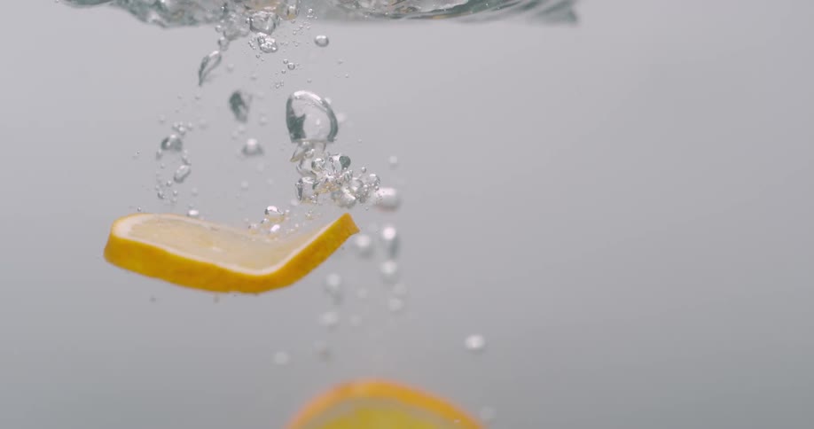 Orange slices plunge into clear liquid leaving a trail of bubbles