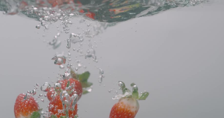Strawberroes fall into water leavin trail of bubbles