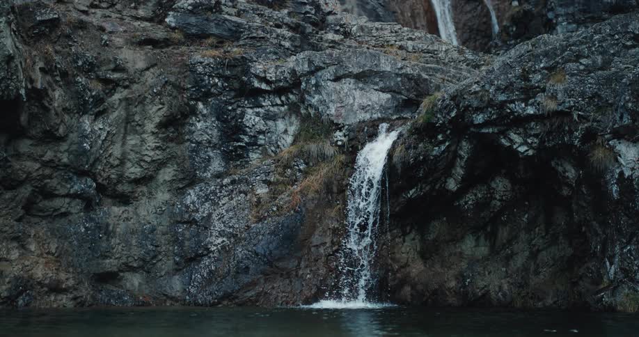Waterfall flows over stone cliffside into lake