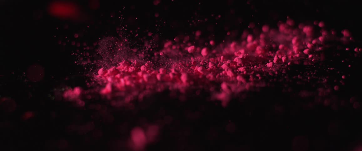 A red powder reacts to an impact on the dark surface