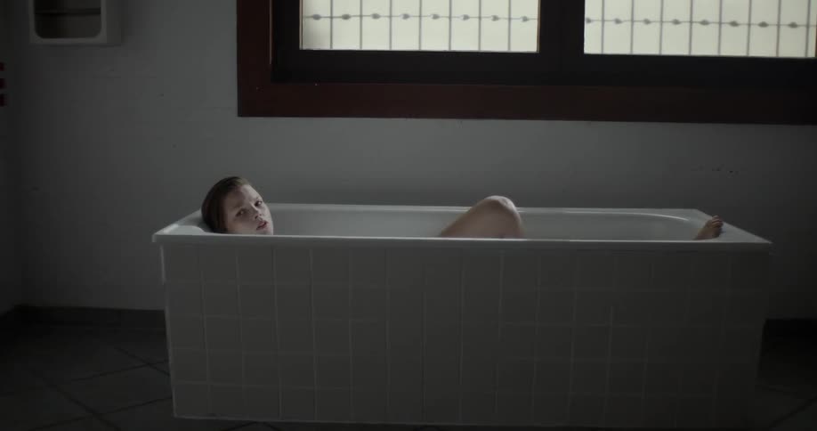 Woman taking bath in bathtub turns to look at the camera