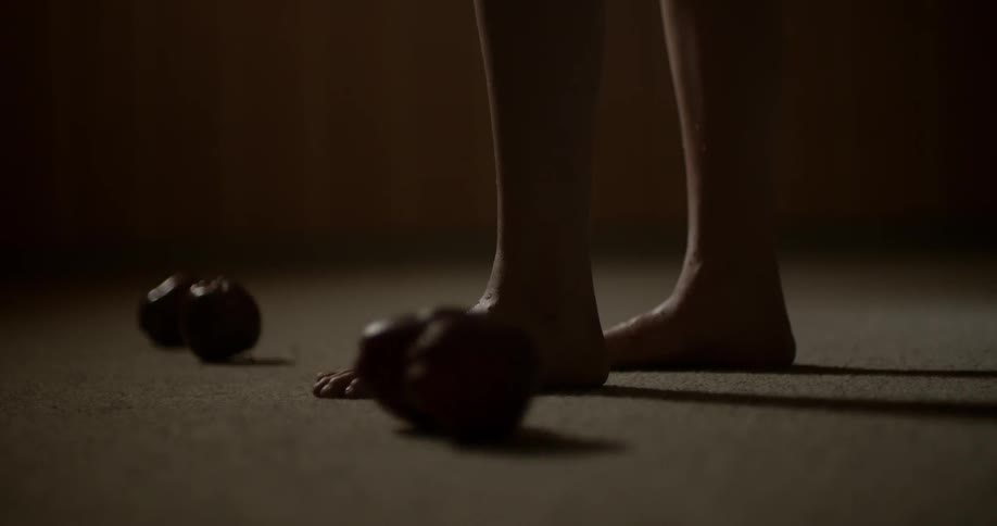 A barefoot person standing on a carpet as apples roll around their feet
