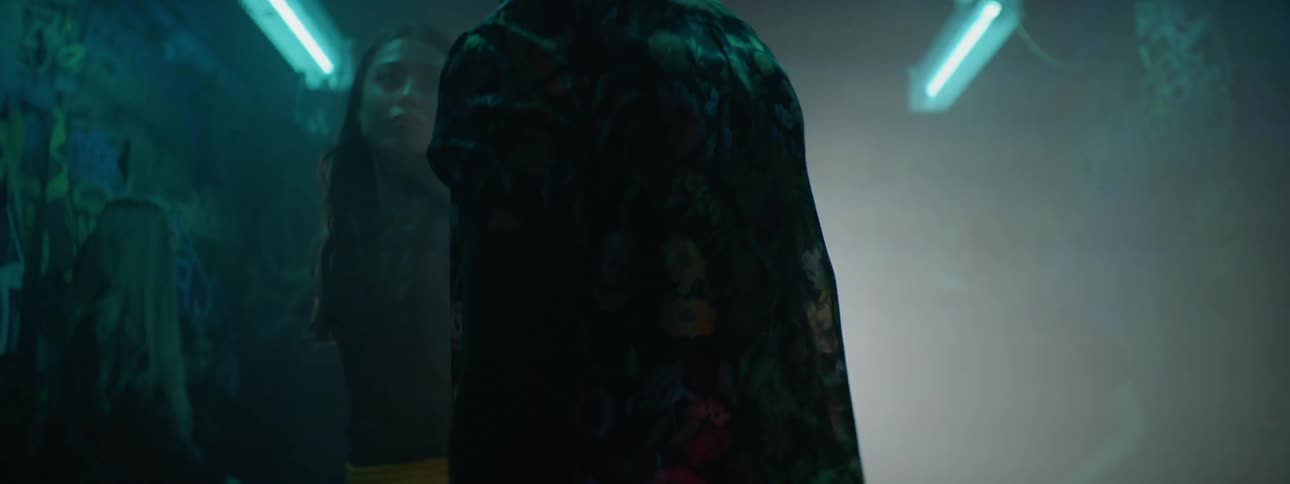 A young woman and man walk together through a dark night club with strobing lights