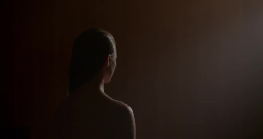 A young woman covered in droplets of water stands in a dimly lit room