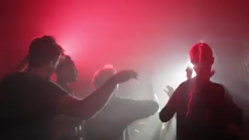 Crowd dance in dark graffiti decorated room under blinking lights