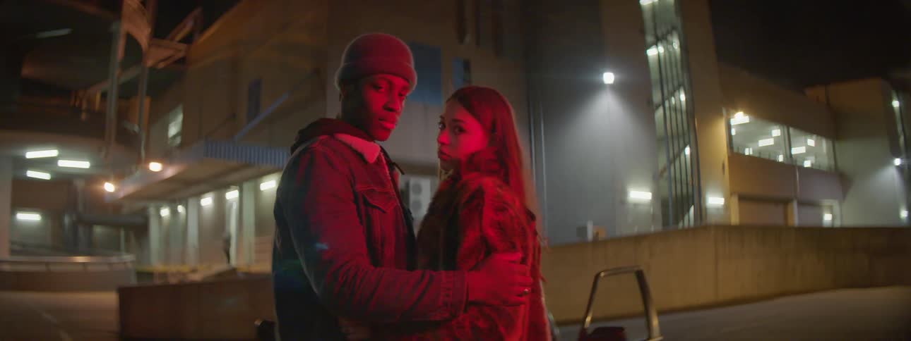 Couple standing in the streets under red lights looking at camera at night
