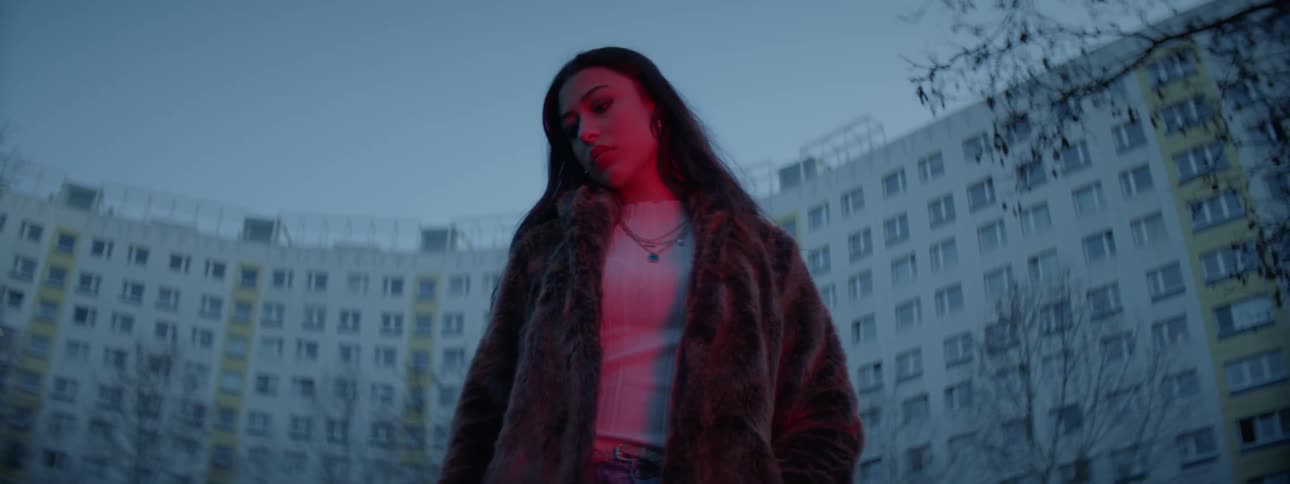 Woman stands outdoors in front of large apartment building