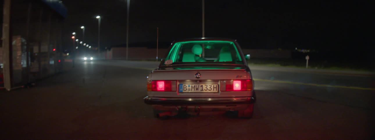 A male turns the wheel of a car and drives toward the highway