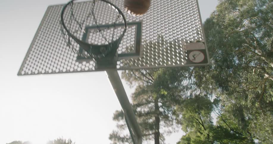 A tall young male dribbles a basketball and then lays it up into an outdoor basketball hoop