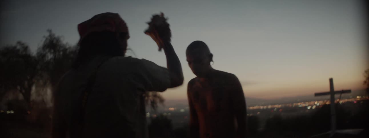 Two people stand near a camp fire on a hilltop at dusk