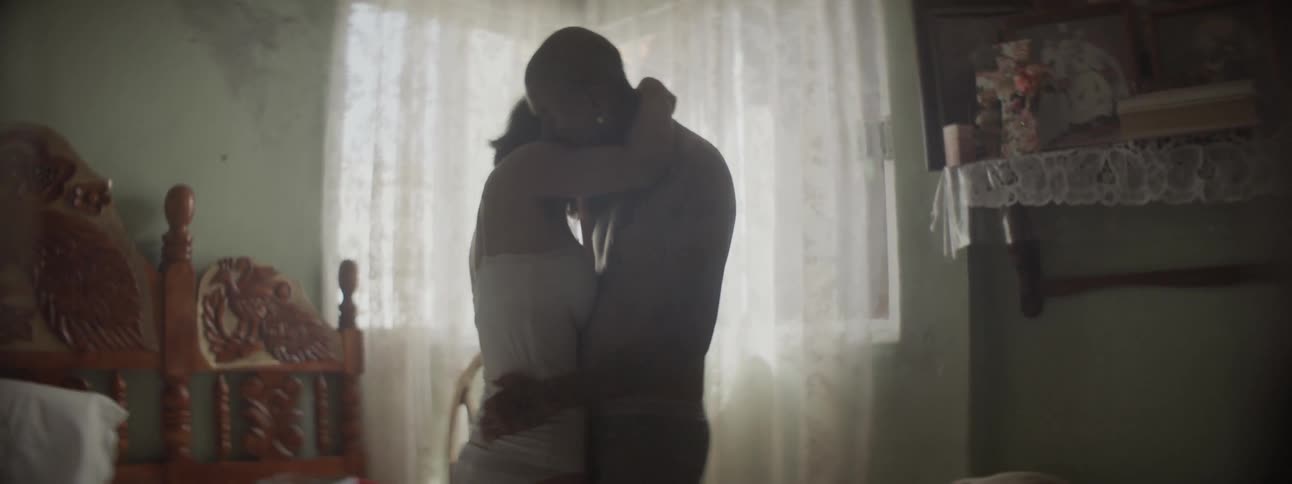 A young man and young woman in their underwear stand and embrace each other within a bedroom
