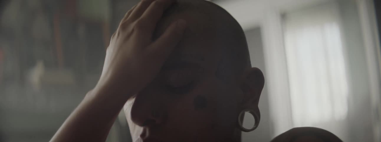 A young woman places her hand on the forehead of a heavily tattooed male