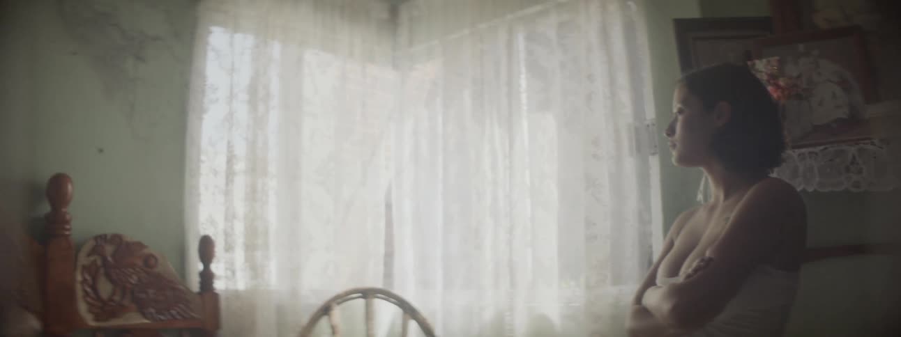 A woman looks out of a window then to a man sitting on an ornate bed