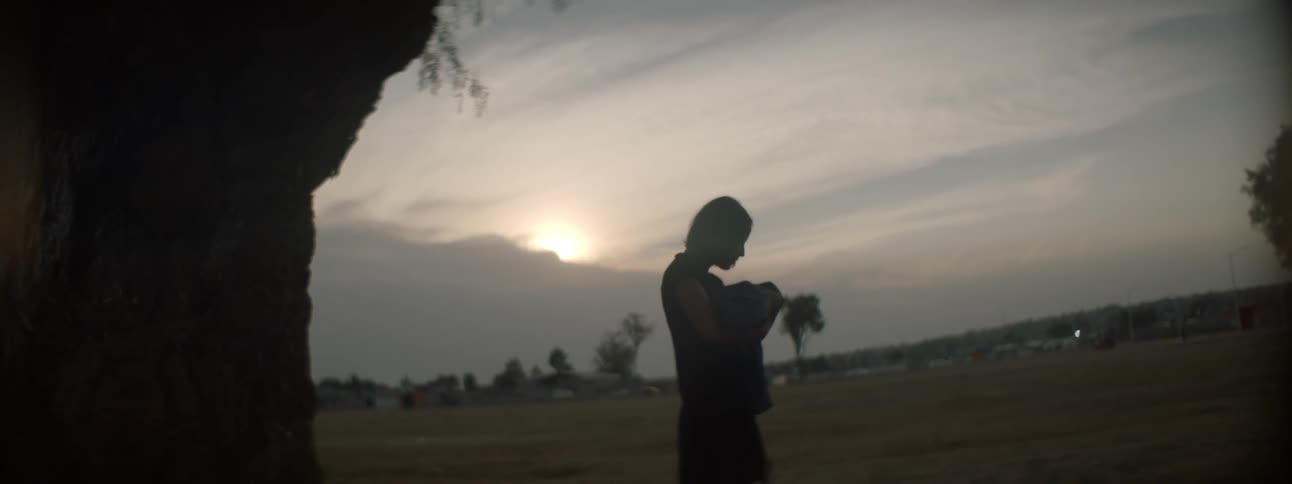 A woman standing outside holding a baby with the sky in the background