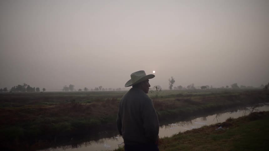 White old man with cowboy hat walking along a river in a rural environment