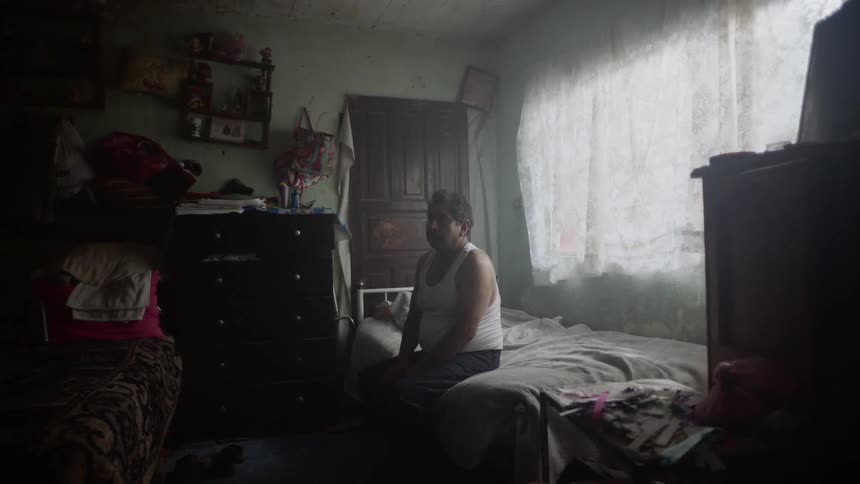 A man sitting in a bed with a window behind him
