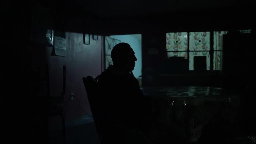 A elderly man sits in the dark as lightning flashes