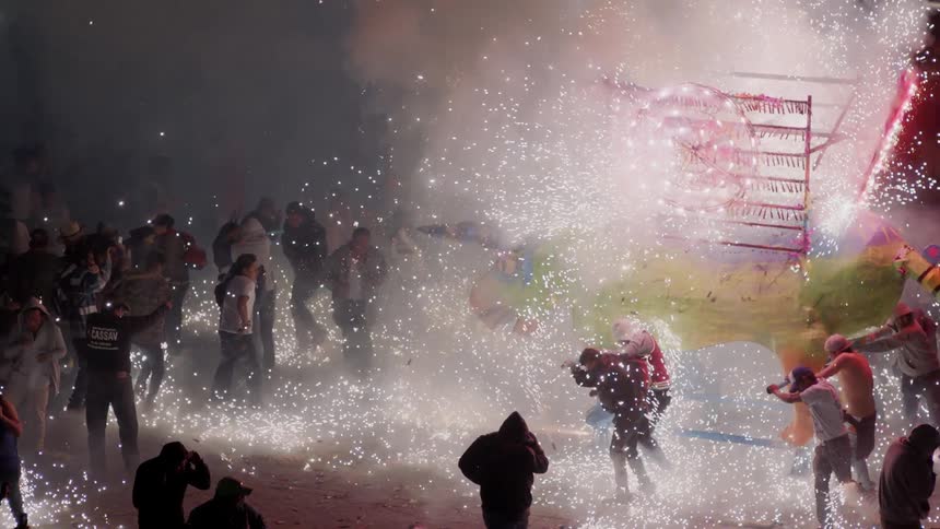 A crowd is gathered around a large bull sculpture being pushed around that is shooting fireworks in all directions