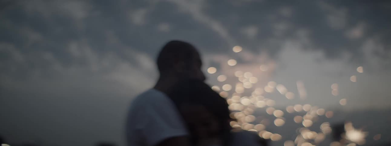 Couple kissing and hugging outdoors in front of fireworks at sunset