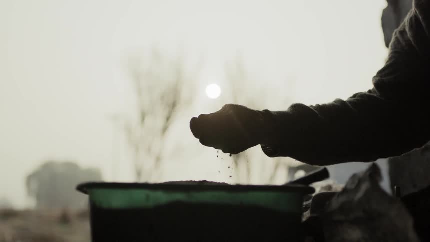 A person crumbles soil in their hands as it falls in a bucket