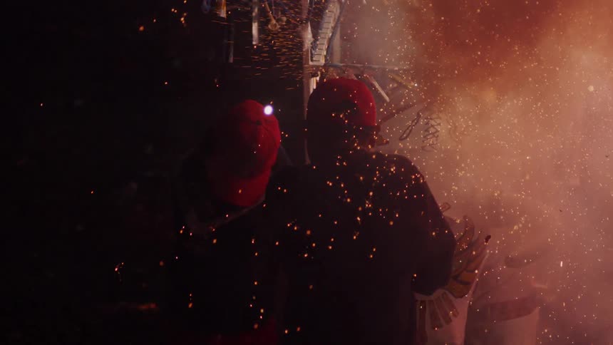 Two men set off fireworks attached to a post
