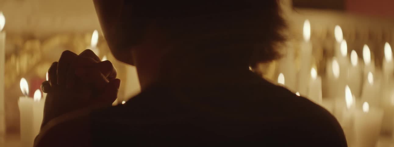 A woman sits and prays in front of candles