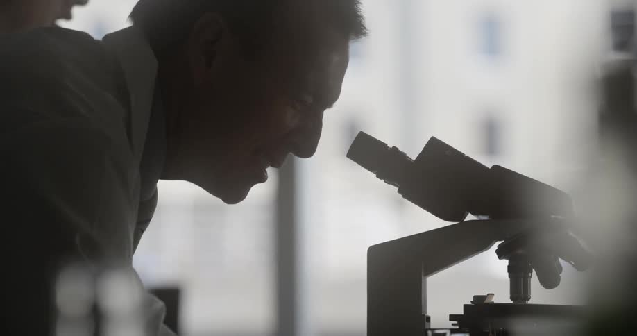 A man leans down to look in a microscope