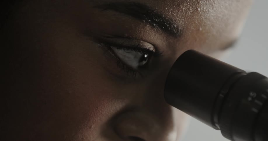 Woman blinks her eye as she looks through a microscope