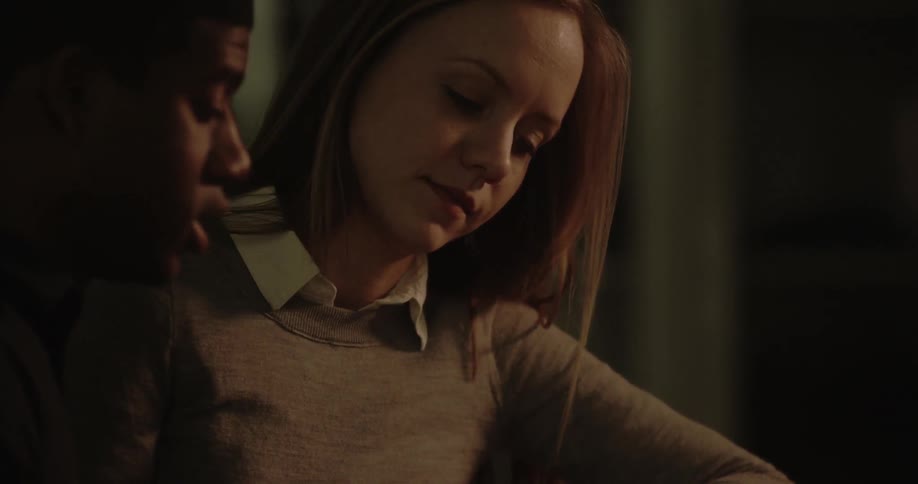A young woman and man sit in a darkened room while having a discussion
