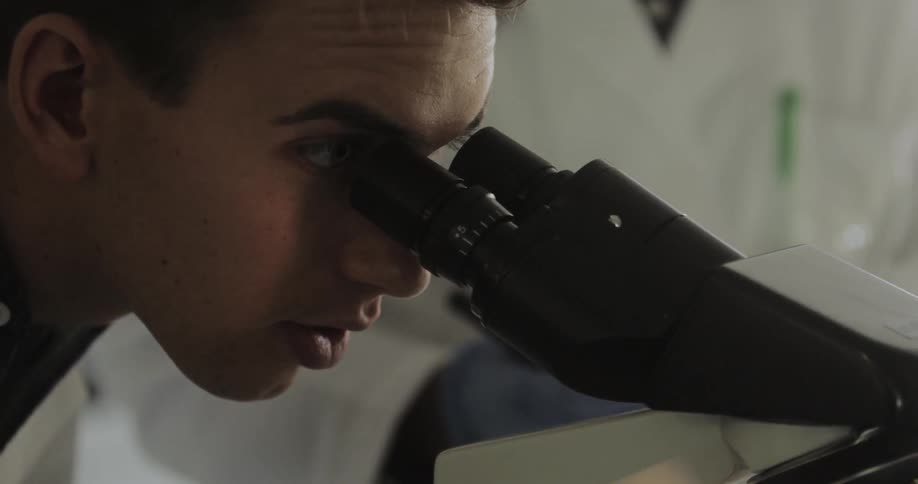 Researcher studying slides a microscope in a lab