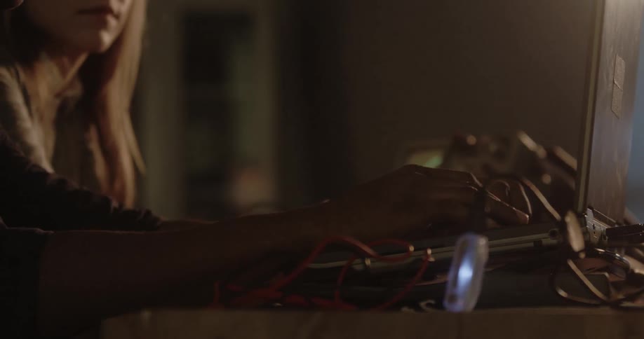 A man types at a computer surrounded by cords