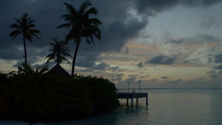 Panoramic view of pier next to hut under palm trees in tropical beach at sunset
