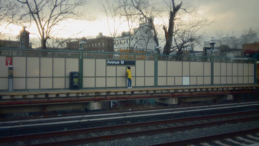 Person wearing yellow hoodie stands near wall on platform near train tracks