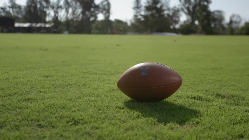 A football is lying on a grass field before being picked up