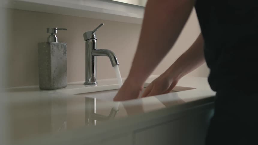 A ma turns on the faucet in the bathroom to wash his hands and adds soap from a dispenser