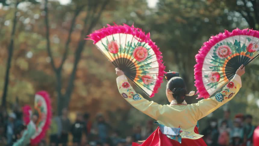 Dancers hold large colorful fans as they turn in a park