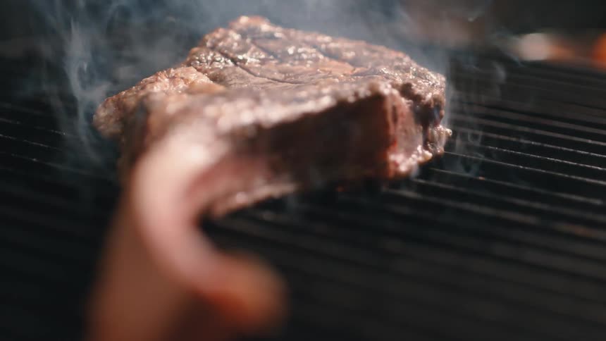 A person grabs the bone of a lamb chop and flips it over on a grill