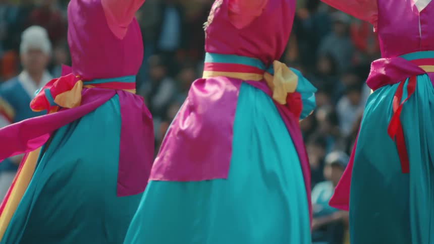 Women in colorful outfits perform playing drums in front of a crowd outdoors